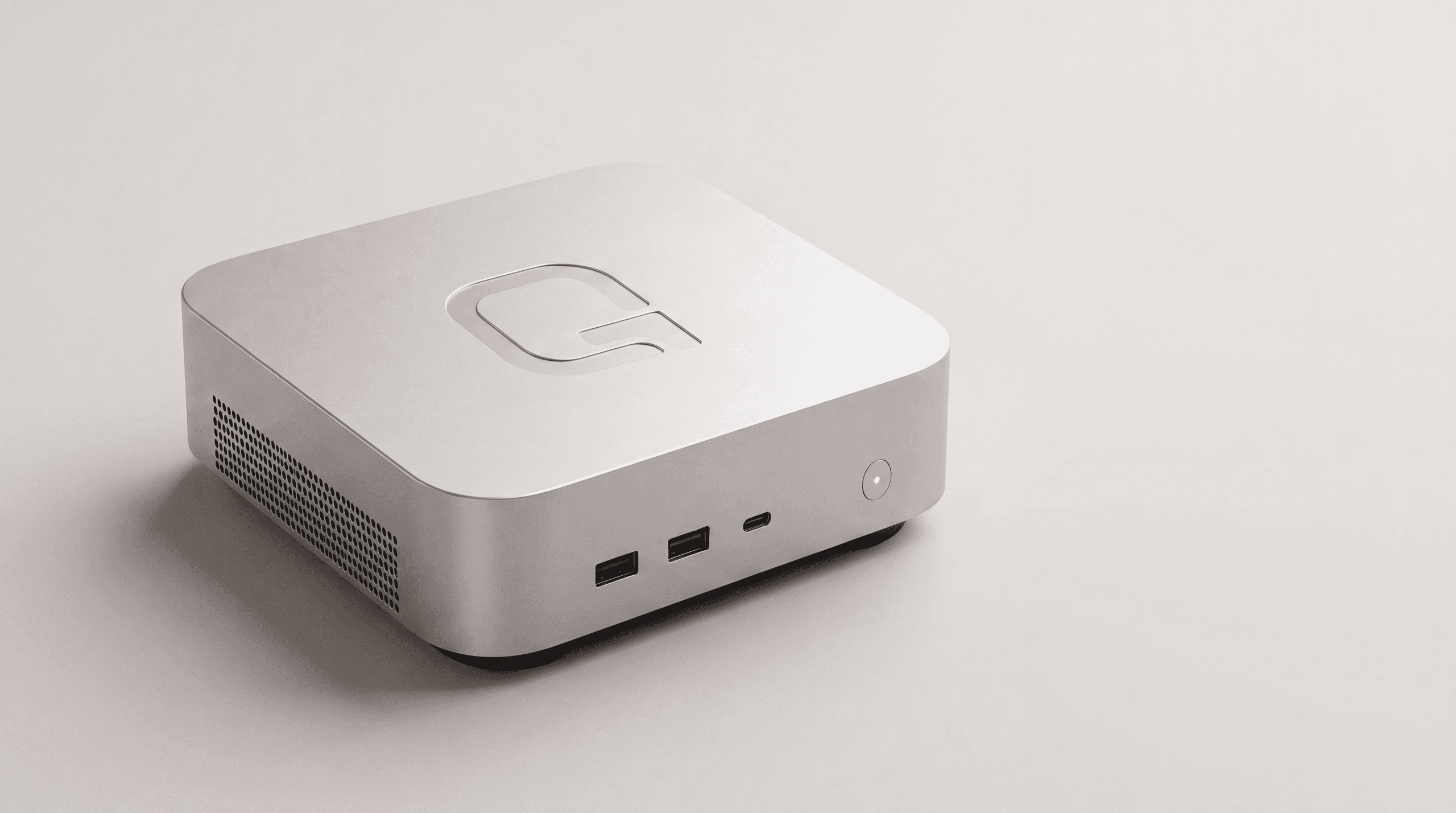 The Qubbo device: a small square aluminum computer in silver, with rounded edges, a debossed Q on the lid, two USB-A ports, one USB-C port and a power button on the front face, and a ventilation grille on the side.